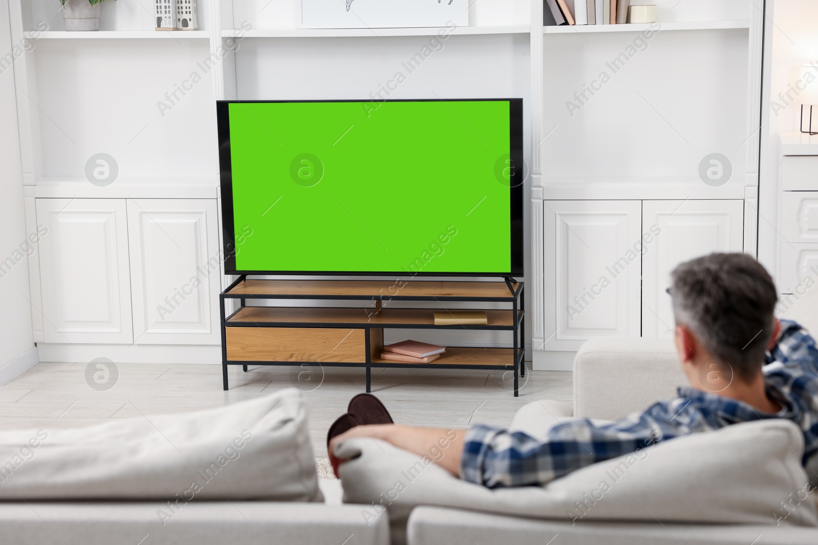 Photo of Man watching TV on sofa at home, back view