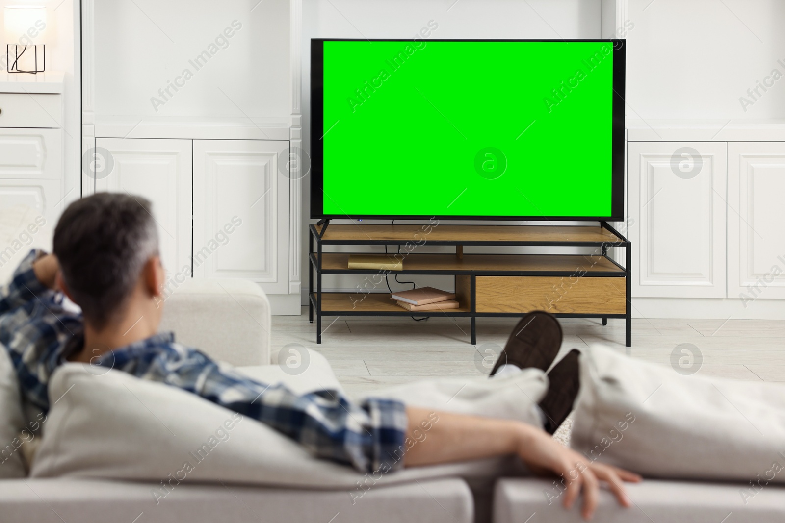 Photo of Man watching TV on sofa at home, back view