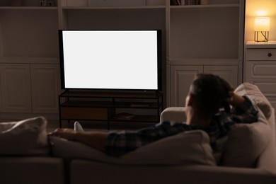 Photo of Man watching TV on sofa at home in evening, back view