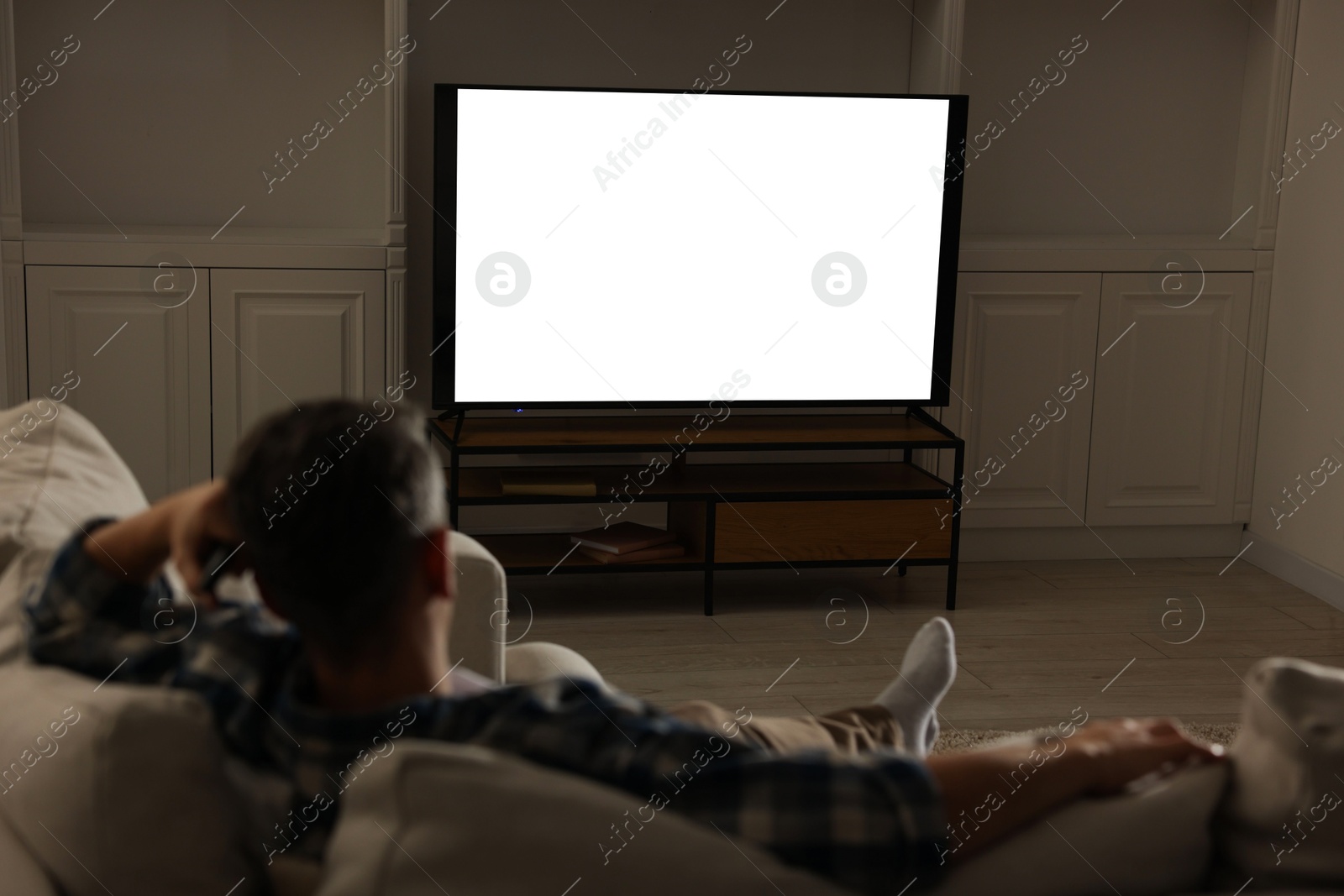 Photo of Man watching TV on sofa at home in evening, back view