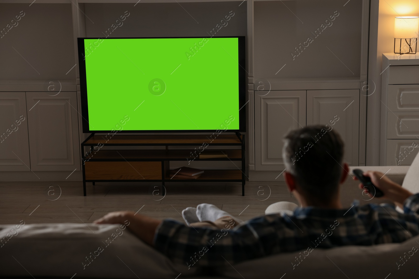 Photo of Man watching TV on sofa at home in evening, back view