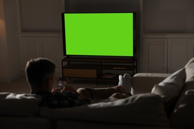 Photo of Man watching TV on sofa at home in evening, back view