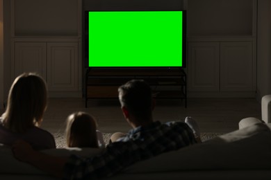 Photo of Family watching TV on sofa at home in evening, back view