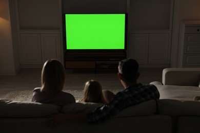 Photo of Family watching TV on sofa at home in evening, back view