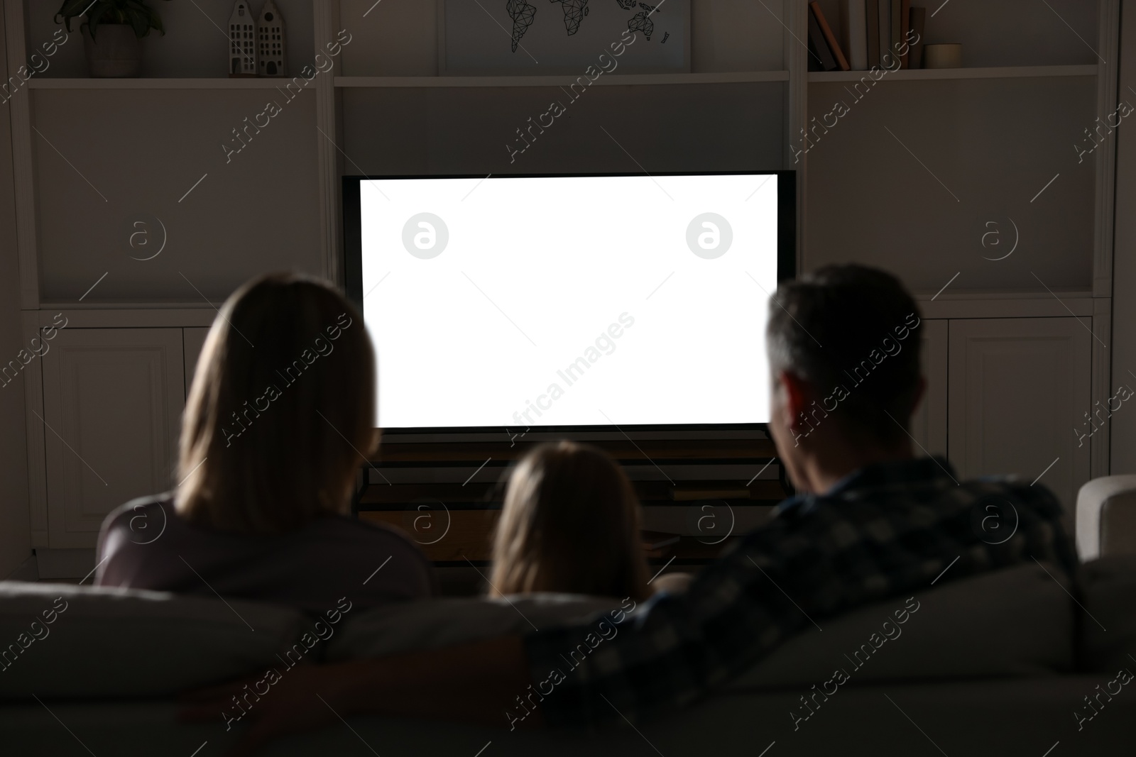 Photo of Family watching TV on sofa at home in evening, back view