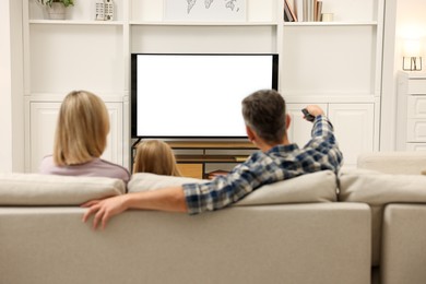 Photo of Family watching TV on sofa at home, back view