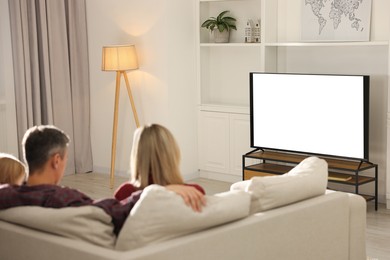 Photo of Family watching TV on sofa at home, back view