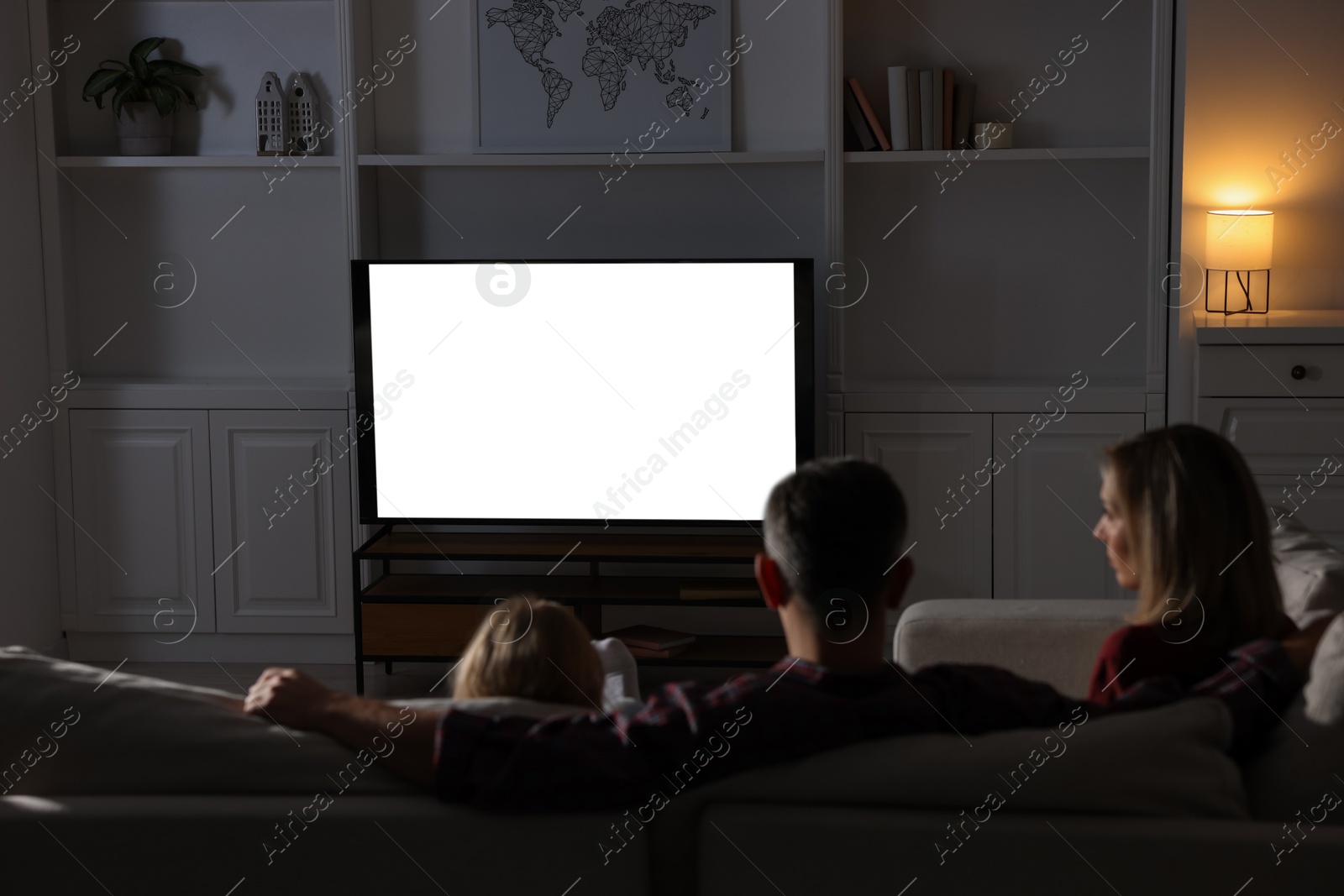 Photo of Family watching TV on sofa at home in evening