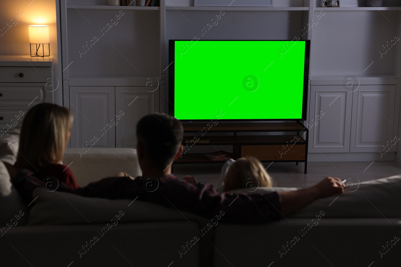 Photo of Family watching TV on sofa at home in evening, back view