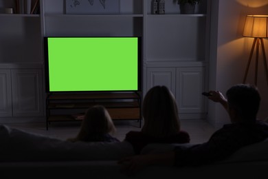 Photo of Family watching TV on sofa at home in evening, back view