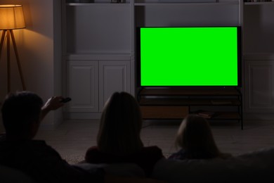 Photo of Family watching TV on sofa at home in evening, back view