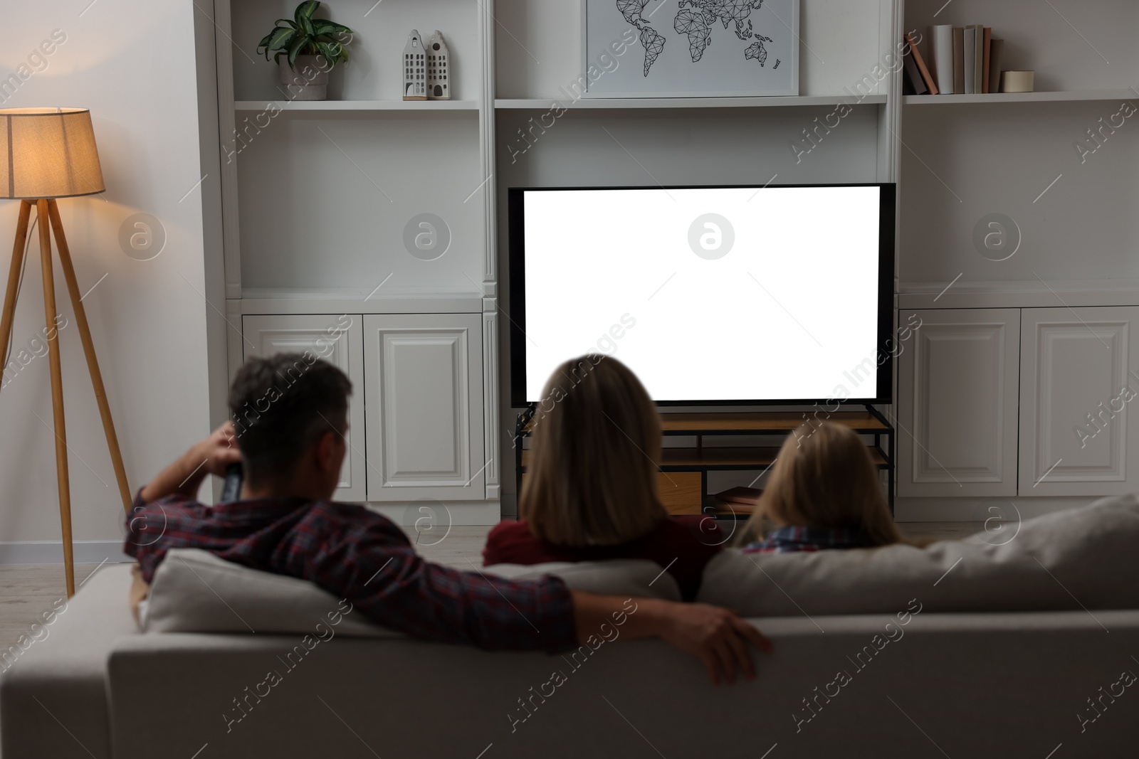 Photo of Family watching TV on sofa at home, back view