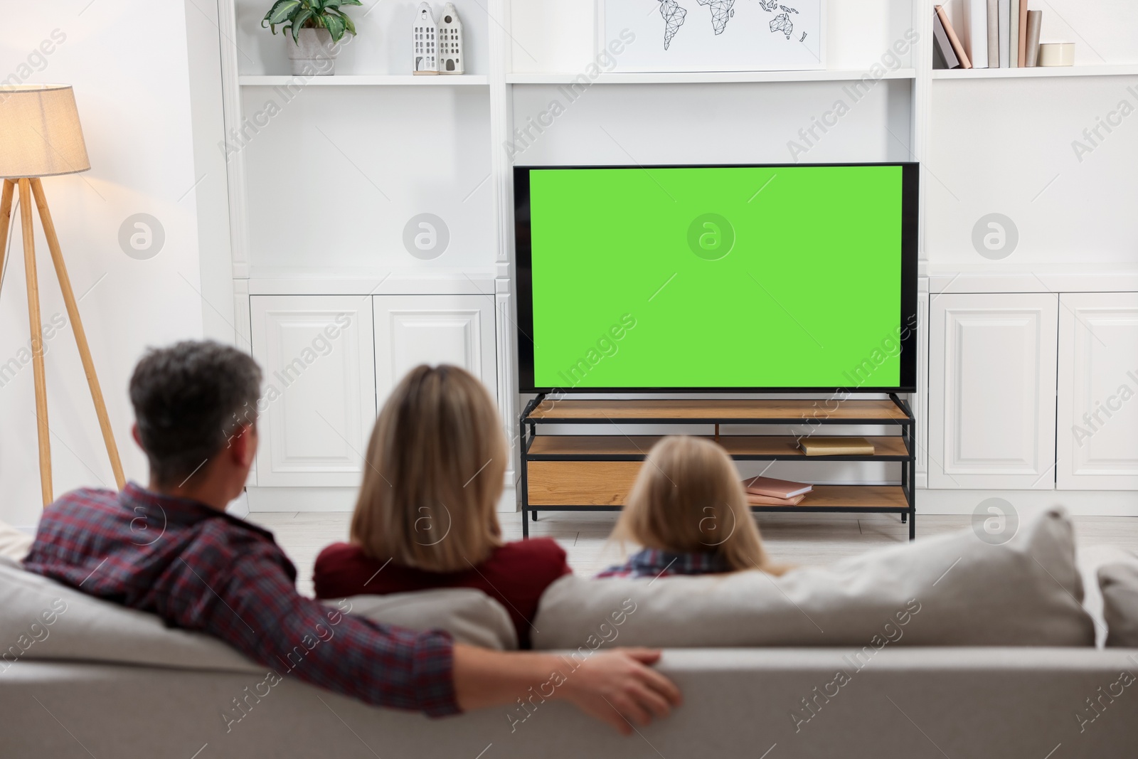 Photo of Family watching TV on sofa at home, back view