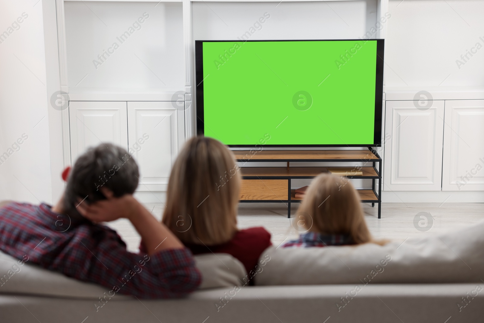 Photo of Family watching TV on sofa at home, back view