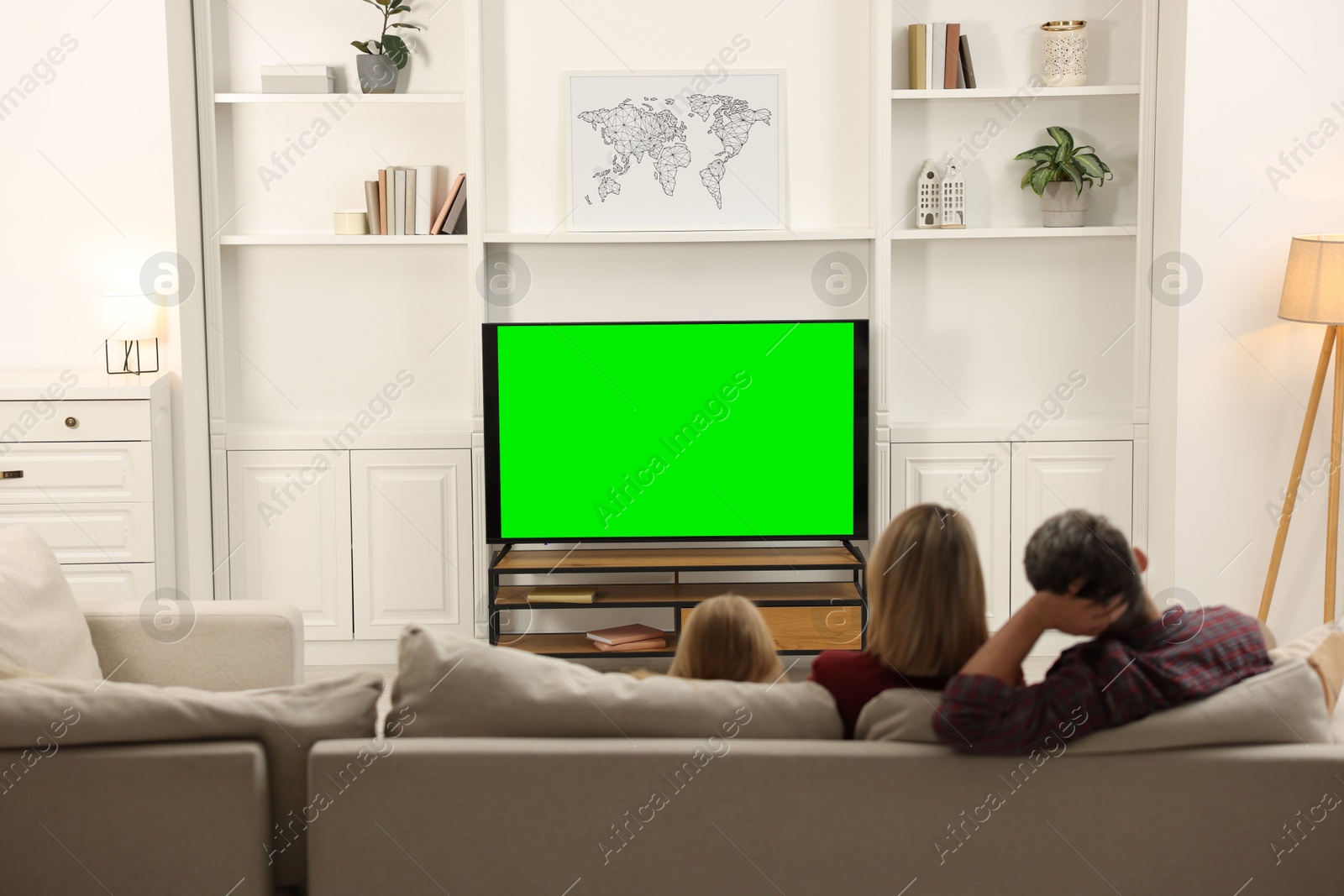 Photo of Family watching TV on sofa at home, back view