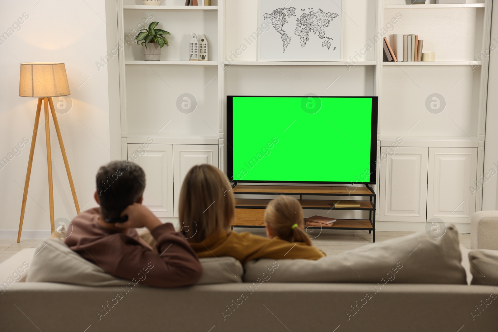 Photo of Family watching TV on sofa at home, back view