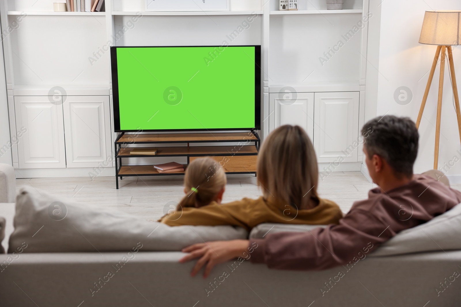 Photo of Family watching TV on sofa at home, back view