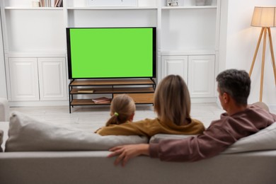 Photo of Family watching TV on sofa at home, back view