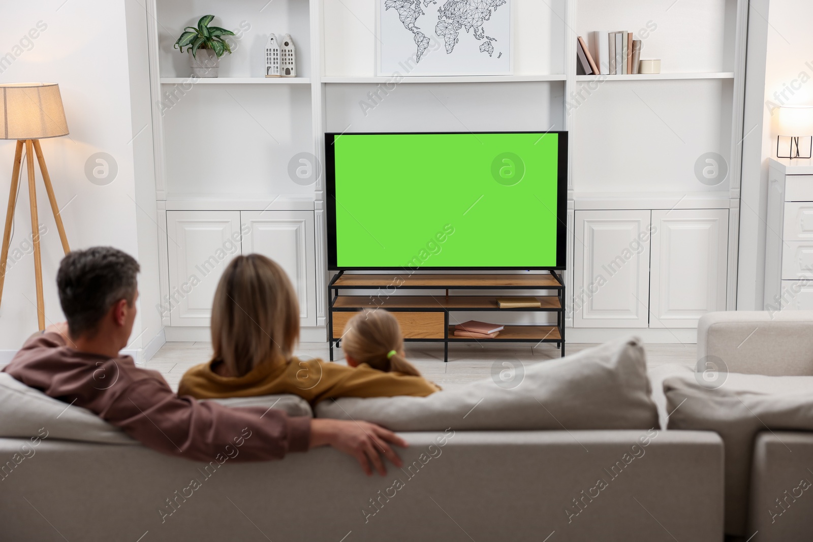 Photo of Family watching TV on sofa at home, back view