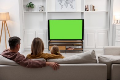 Photo of Family watching TV on sofa at home, back view