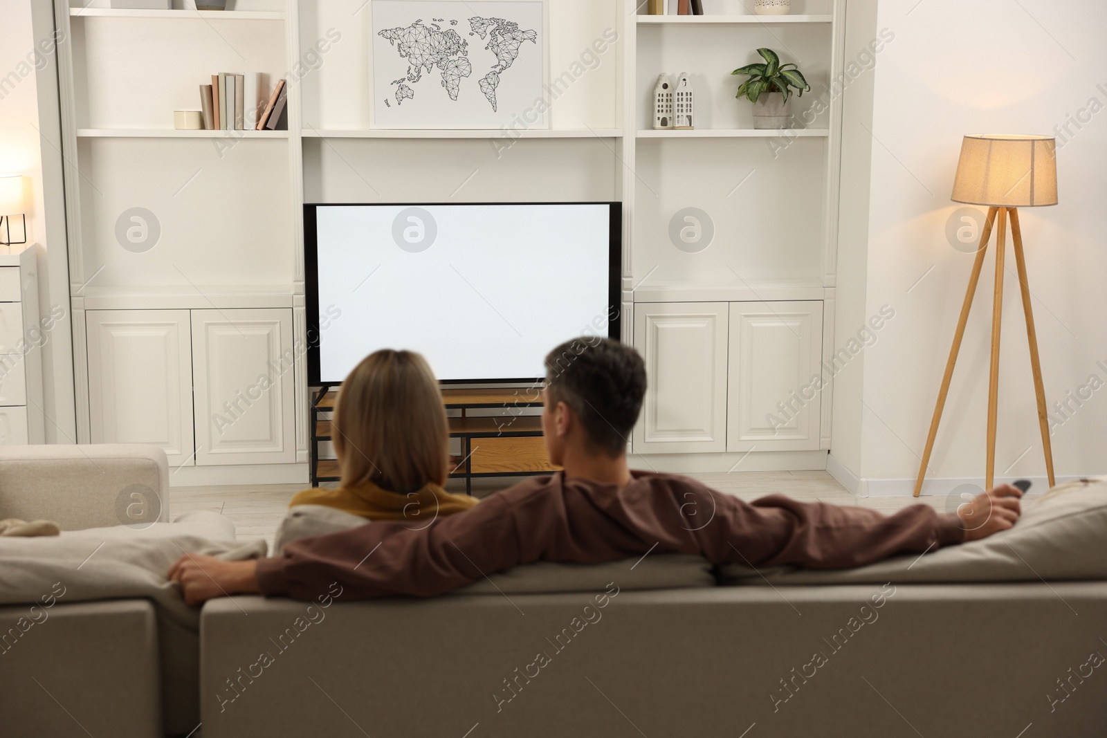 Photo of Couple watching TV on sofa at home, back view