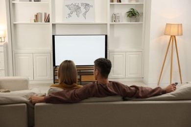 Photo of Couple watching TV on sofa at home, back view