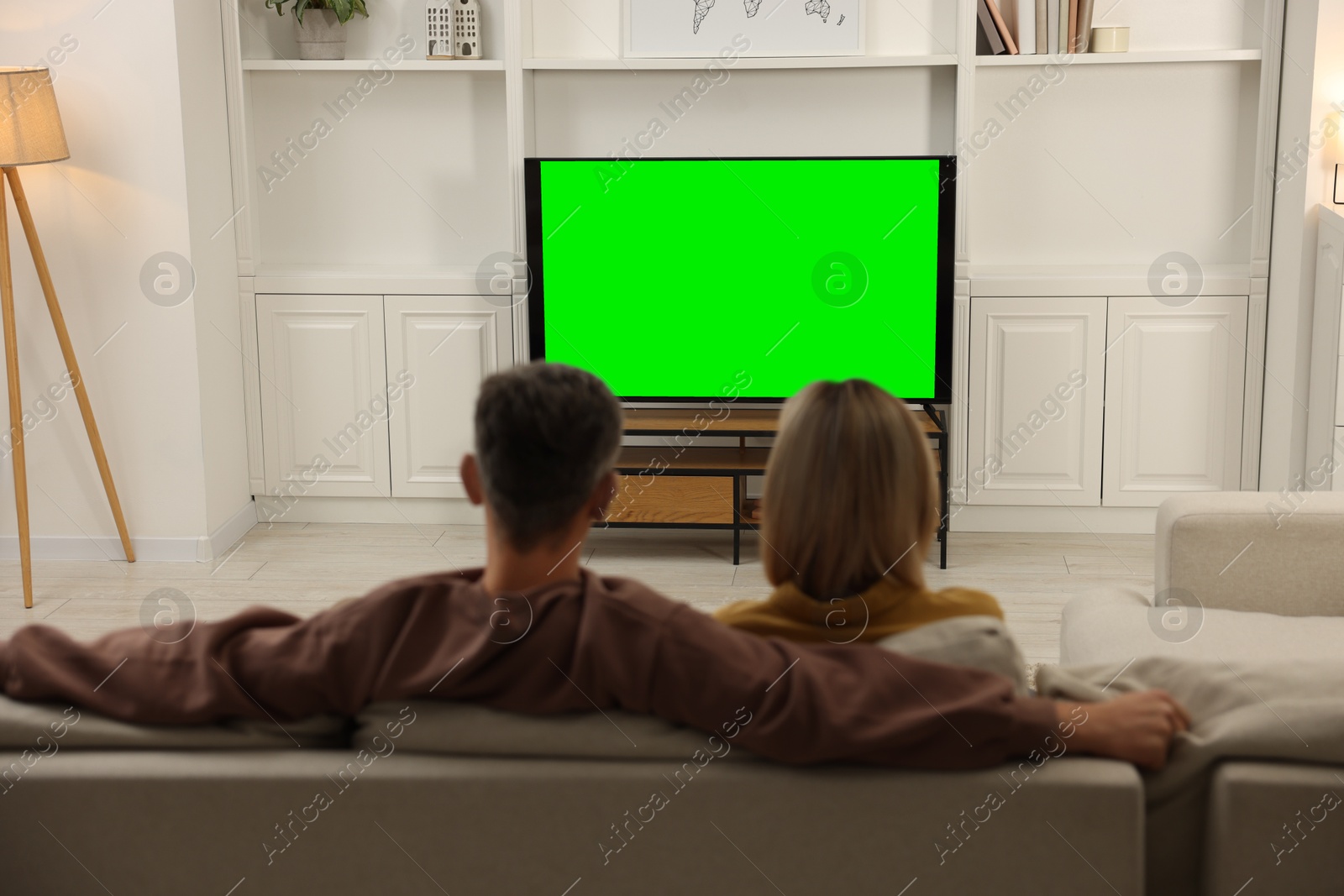 Photo of Couple watching TV on sofa at home, back view