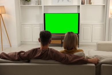 Photo of Couple watching TV on sofa at home, back view