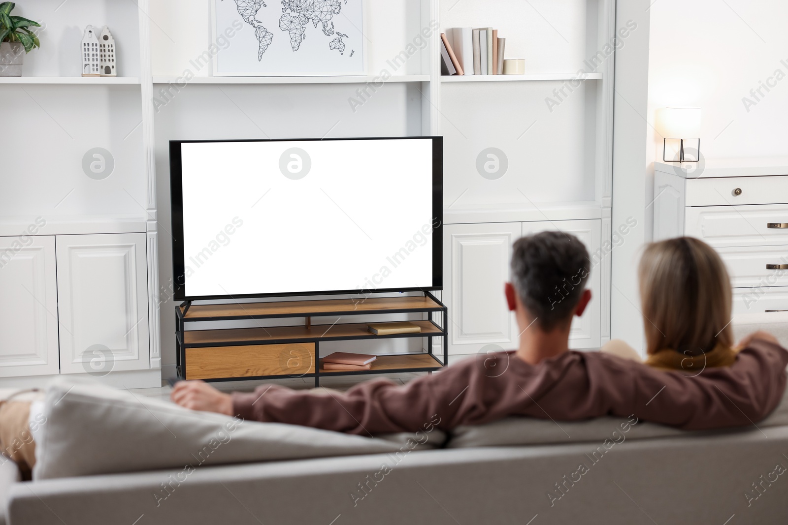 Photo of Couple watching TV on sofa at home, back view