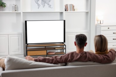 Photo of Couple watching TV on sofa at home, back view