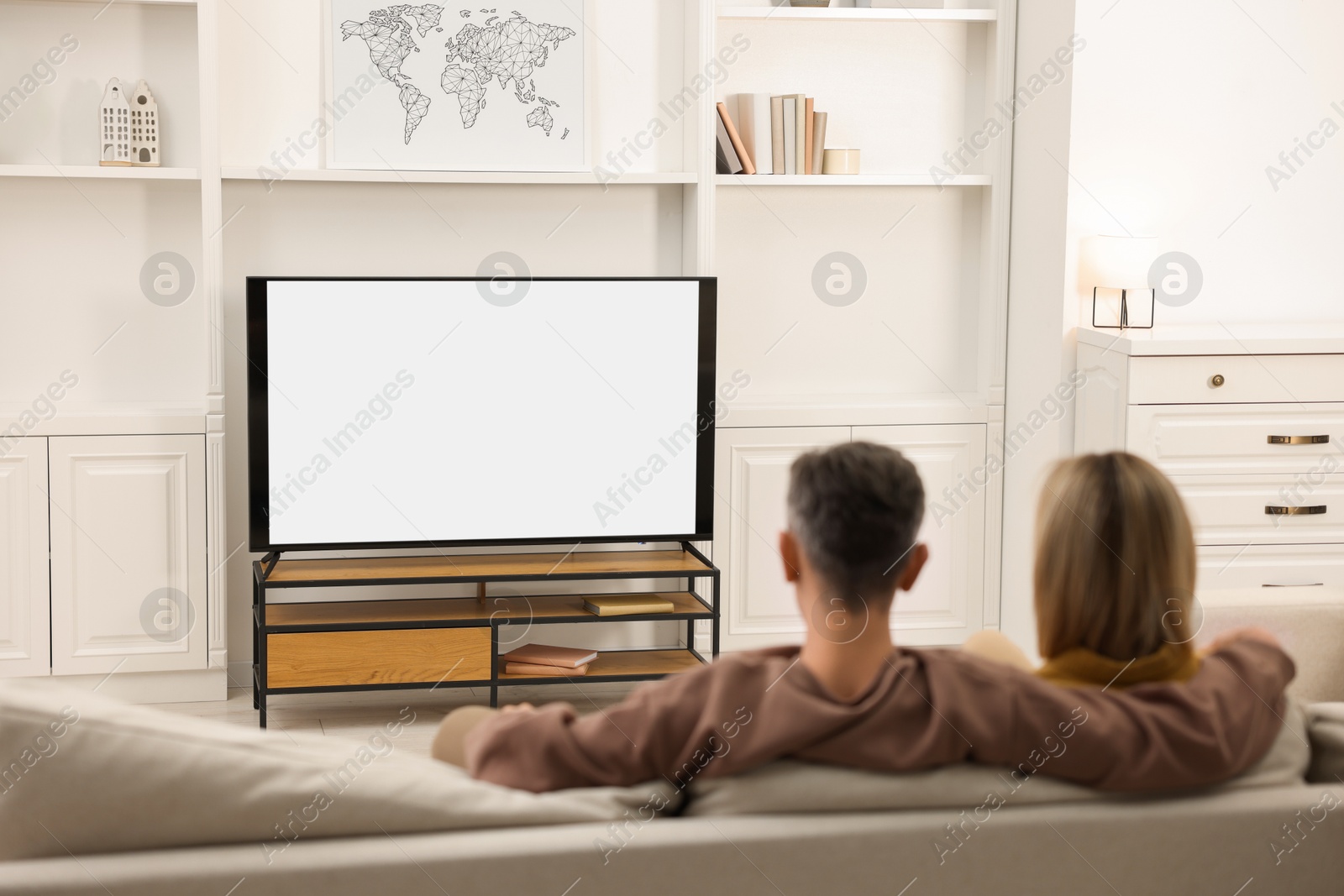 Photo of Couple watching TV on sofa at home, back view