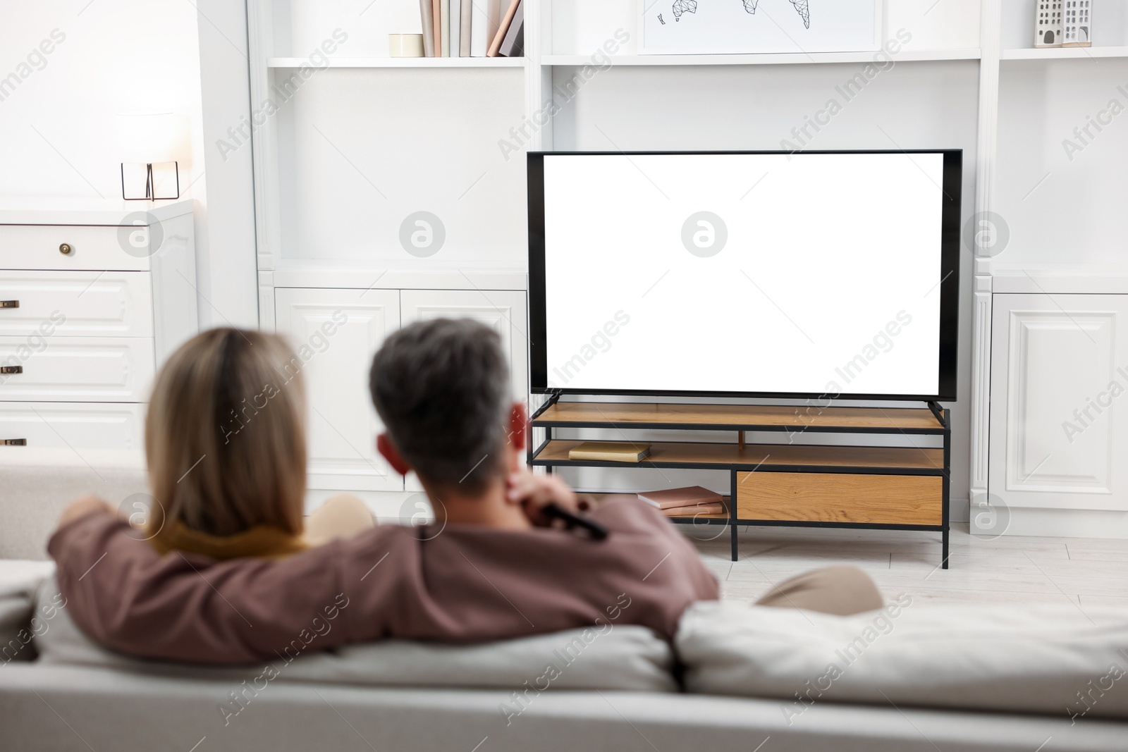 Photo of Couple watching TV on sofa at home, back view