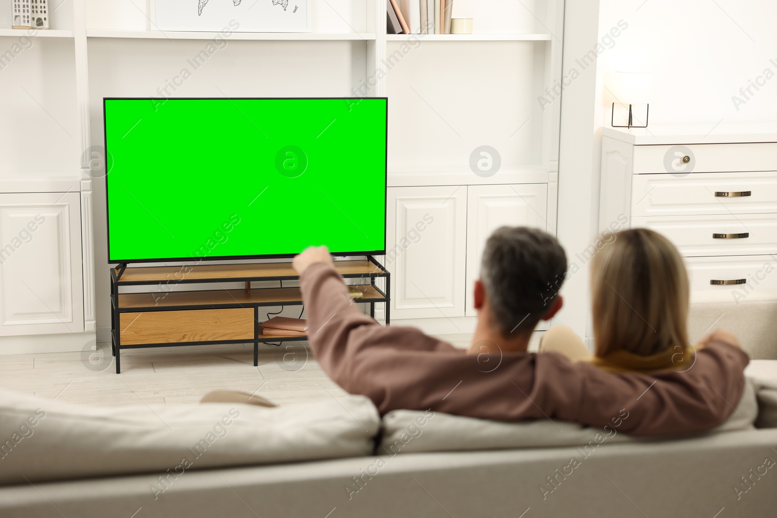 Photo of Couple watching TV on sofa at home, back view