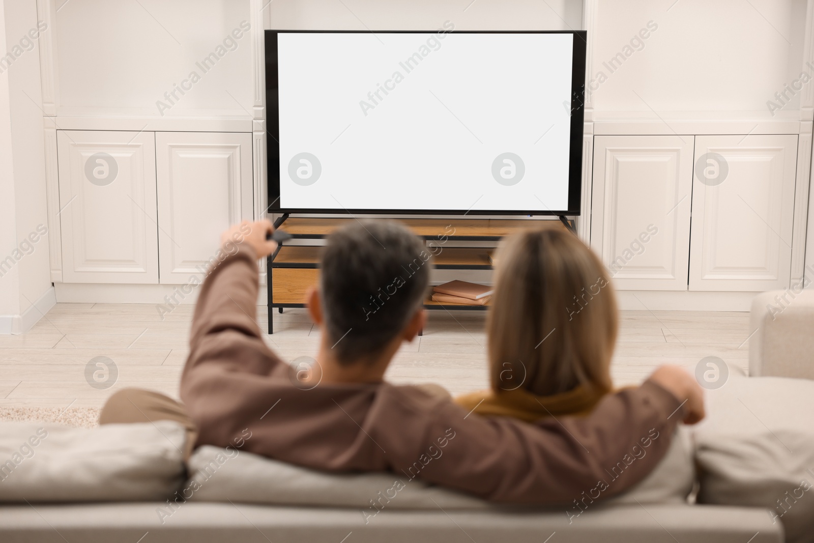 Photo of Couple watching TV on sofa at home, back view