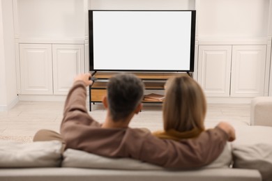 Couple watching TV on sofa at home, back view