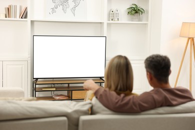 Photo of Couple watching TV on sofa at home, back view