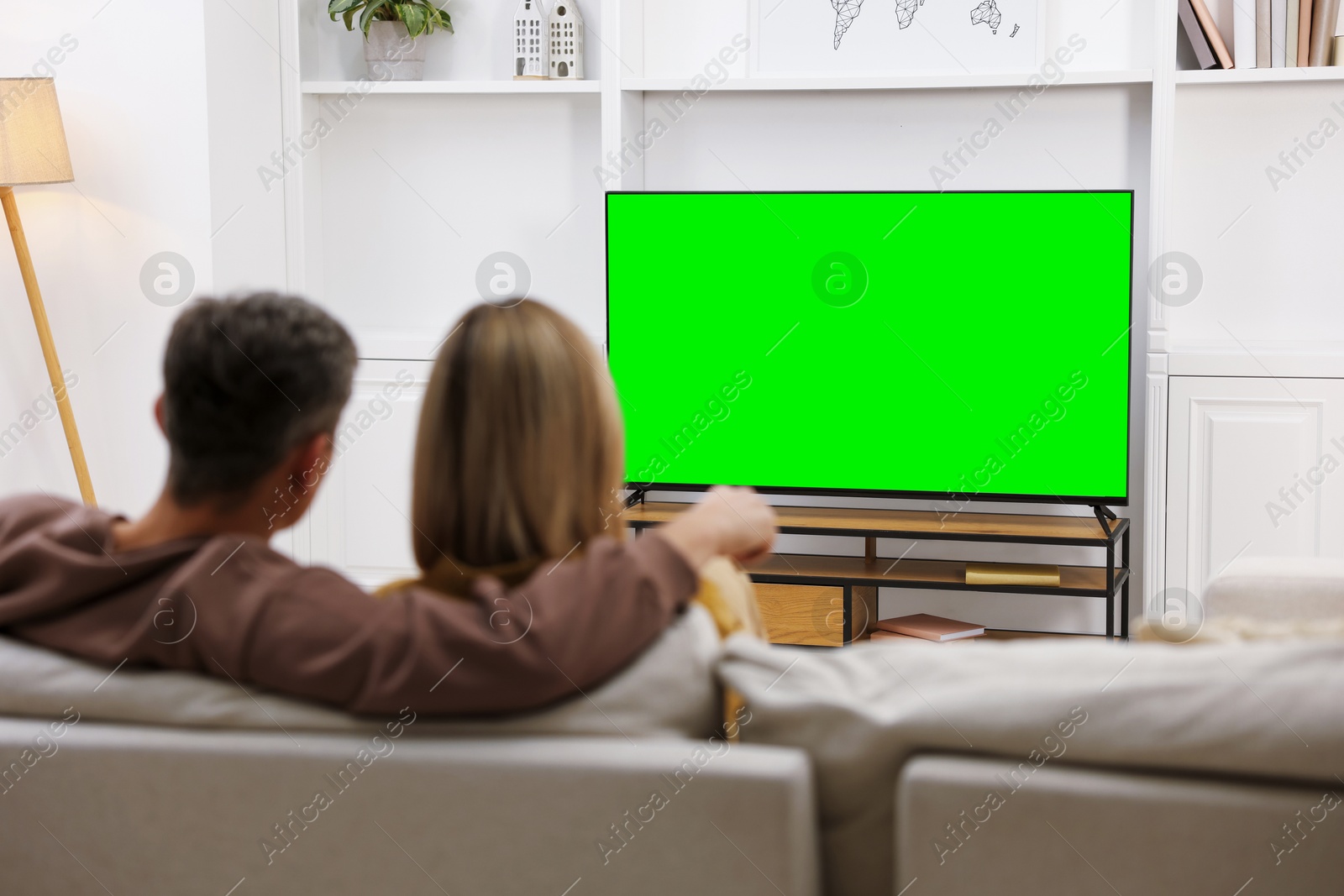 Photo of Couple watching TV on sofa at home, back view