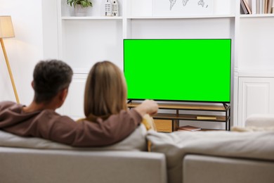 Photo of Couple watching TV on sofa at home, back view