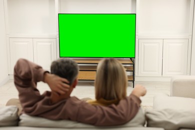 Photo of Couple watching TV on sofa at home, back view