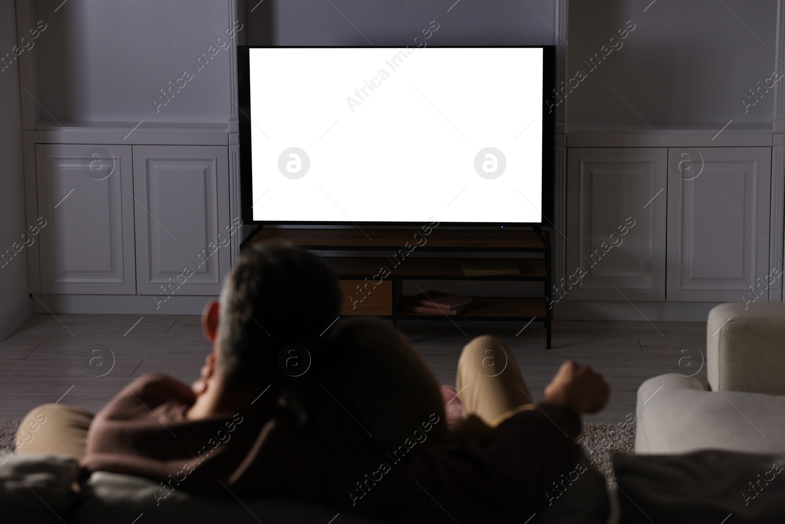 Photo of Couple watching TV on sofa at home in evening, back view