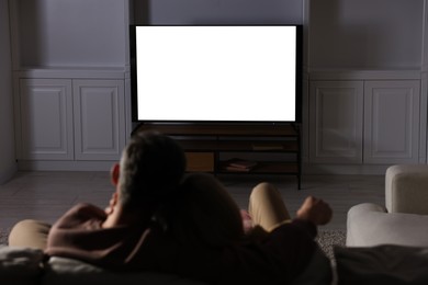 Couple watching TV on sofa at home in evening, back view