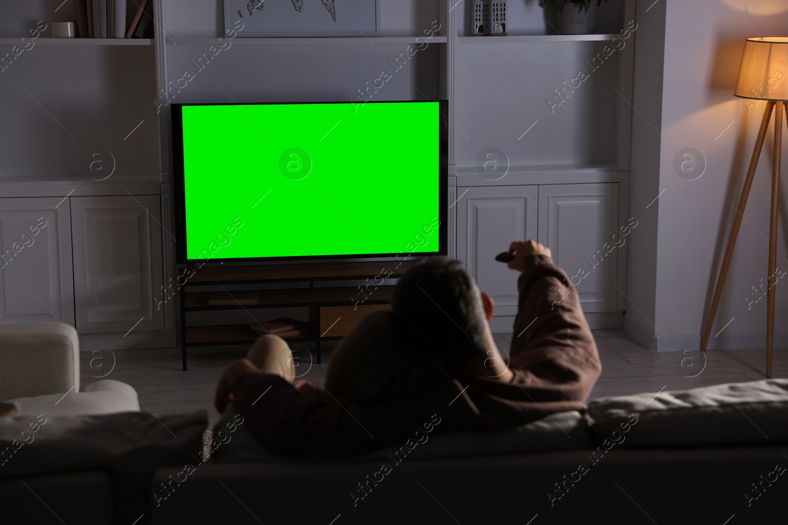 Photo of Couple watching TV on sofa at home in evening, back view