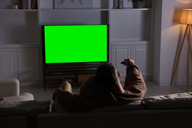 Photo of Couple watching TV on sofa at home in evening, back view