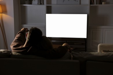 Photo of Couple watching TV on sofa at home in evening, back view