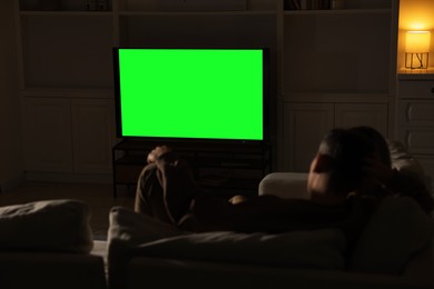 Photo of Couple watching TV on sofa at home in evening, back view