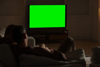 Photo of Couple watching TV on sofa at home in evening, back view