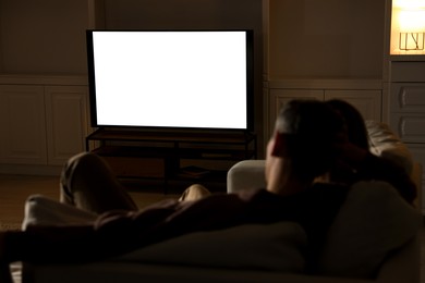 Photo of Couple watching TV on sofa at home in evening, back view