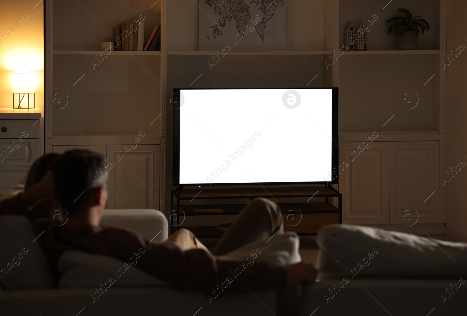 Photo of Couple watching TV on sofa at home in evening, back view