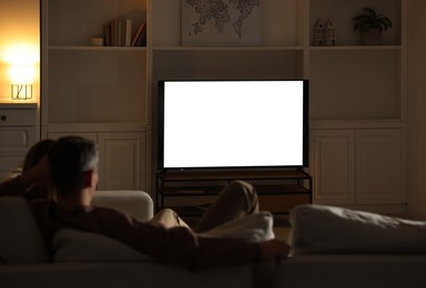 Photo of Couple watching TV on sofa at home in evening, back view