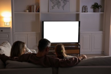 Photo of Family watching TV on sofa at home, back view